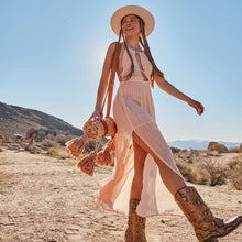 Load image into Gallery viewer, Wandering Folk Picknickdecke Wild Peach | Boho, Wasserdicht ; Farbe: Peach, Rosa ; mit orientalischen Muster; Lifestyle Foto mit zusammengerollter Decke über Schulter in Wüste