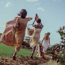 Load image into Gallery viewer, Wandering Folk Woven Throw Rosé | Boho ; Farbe: Rosa, Ockergelb ; mit Fransen ; Blumenmuster ; Lifestyle Foto Decke in Armen laufendes Model im Feld ; Campingdecke