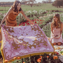 Load image into Gallery viewer, Wandering Folk Woven Throw Rosé | Boho ; Farbe: Rosa, Ockergelb ; mit Fransen ; Blumenmuster ; Lifestyle Foto Decke in Feld ; Campingdecke